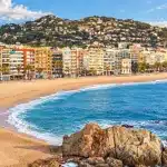La plage de Fenals à Lloret de Mar, bordée par un promontoire boisé.